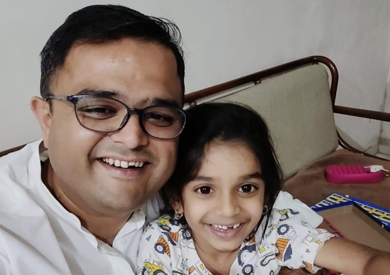 A smiling man in glasses with his arm around a smiling young child