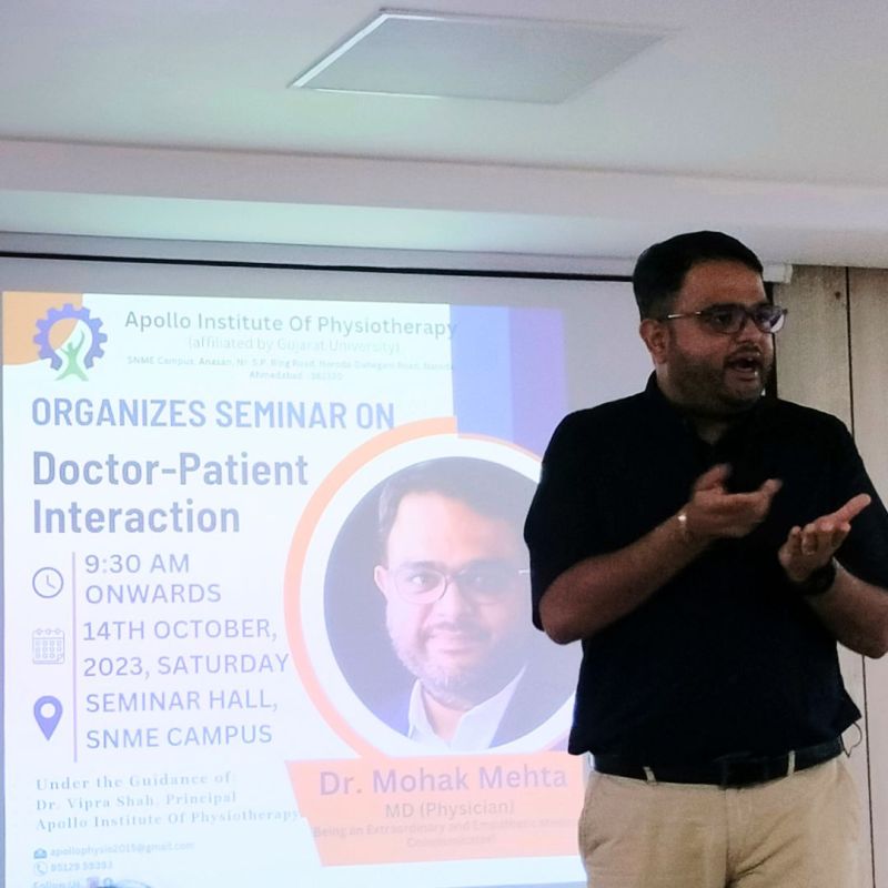 A man in a dark shirt speaking, with a slide behind him announcing a seminar on doctor-patient interaction