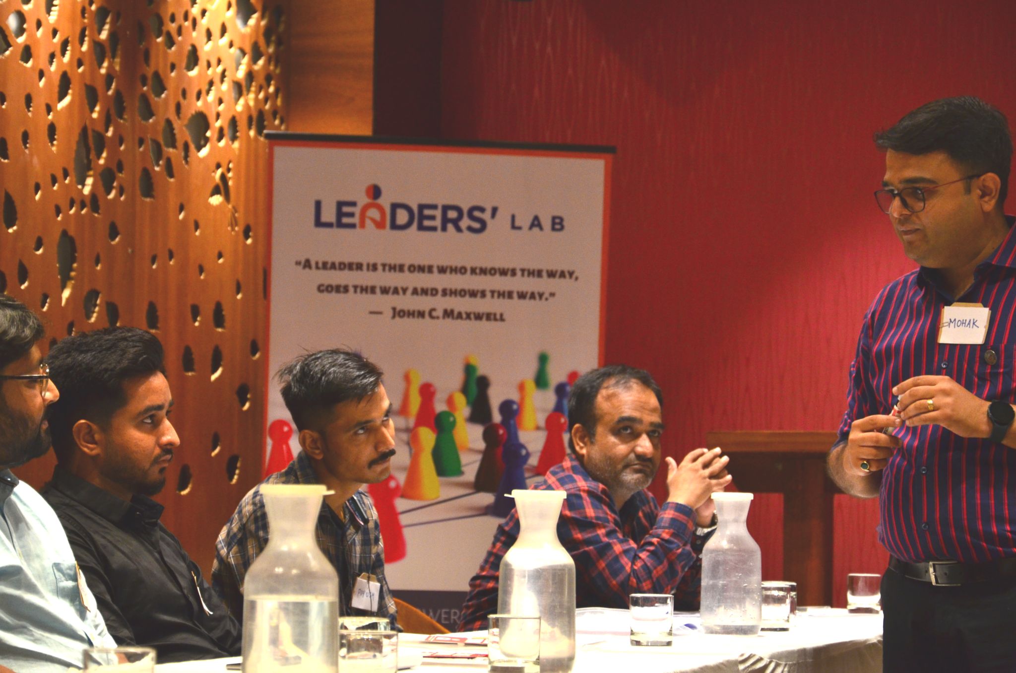 A group seated at a table, listening to a speaker standing at the right