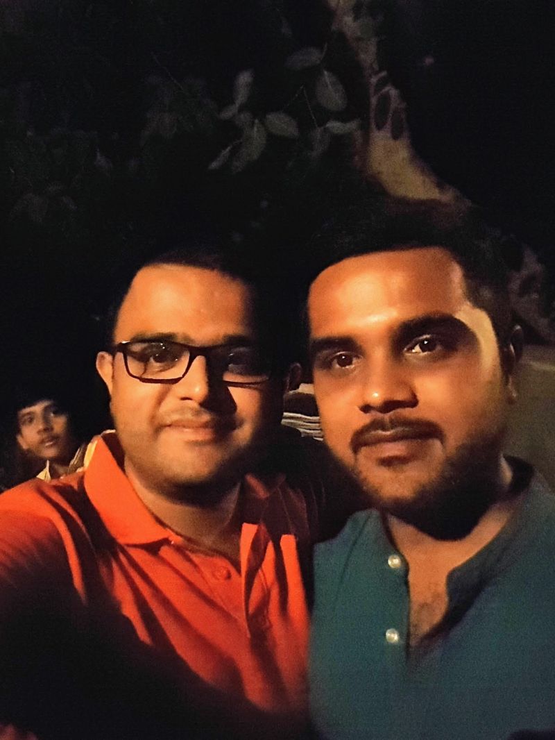 Two men in a close selfie at night, one in glasses and an orange shirt, the other bearded in a green shirt