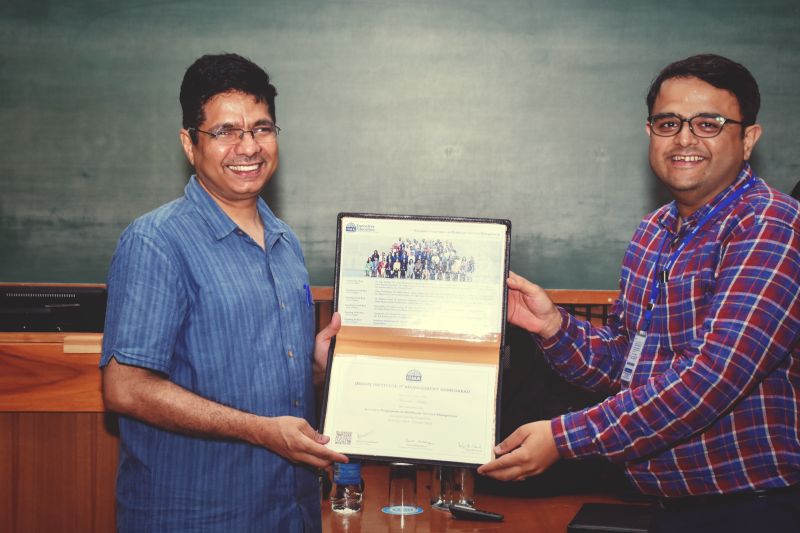 Two men smiling and holding a framed certificate from the Indian Institute of Management Ahmedabad