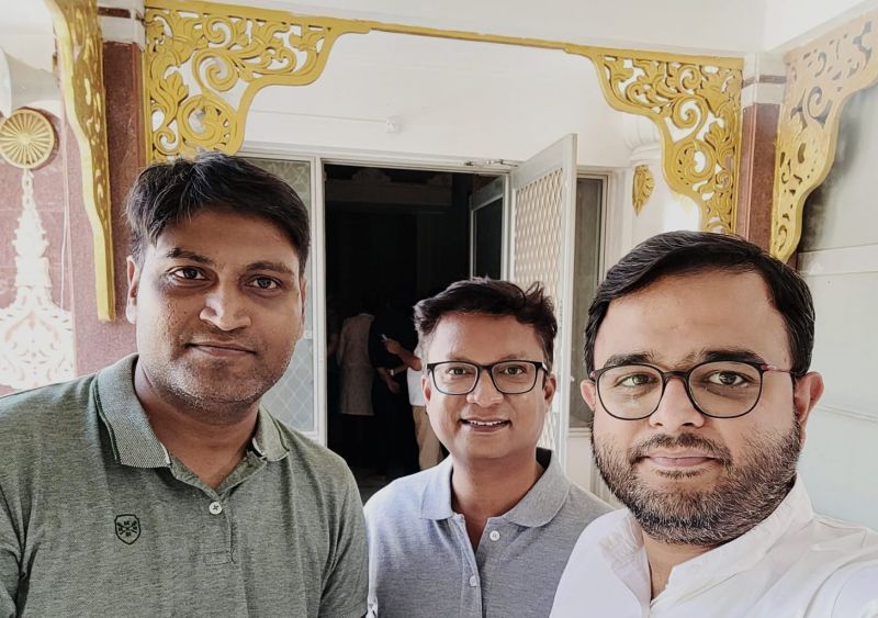 Three men smiling in a selfie in front of an ornate golden doorway at the Vipassana centre in Igatpuri