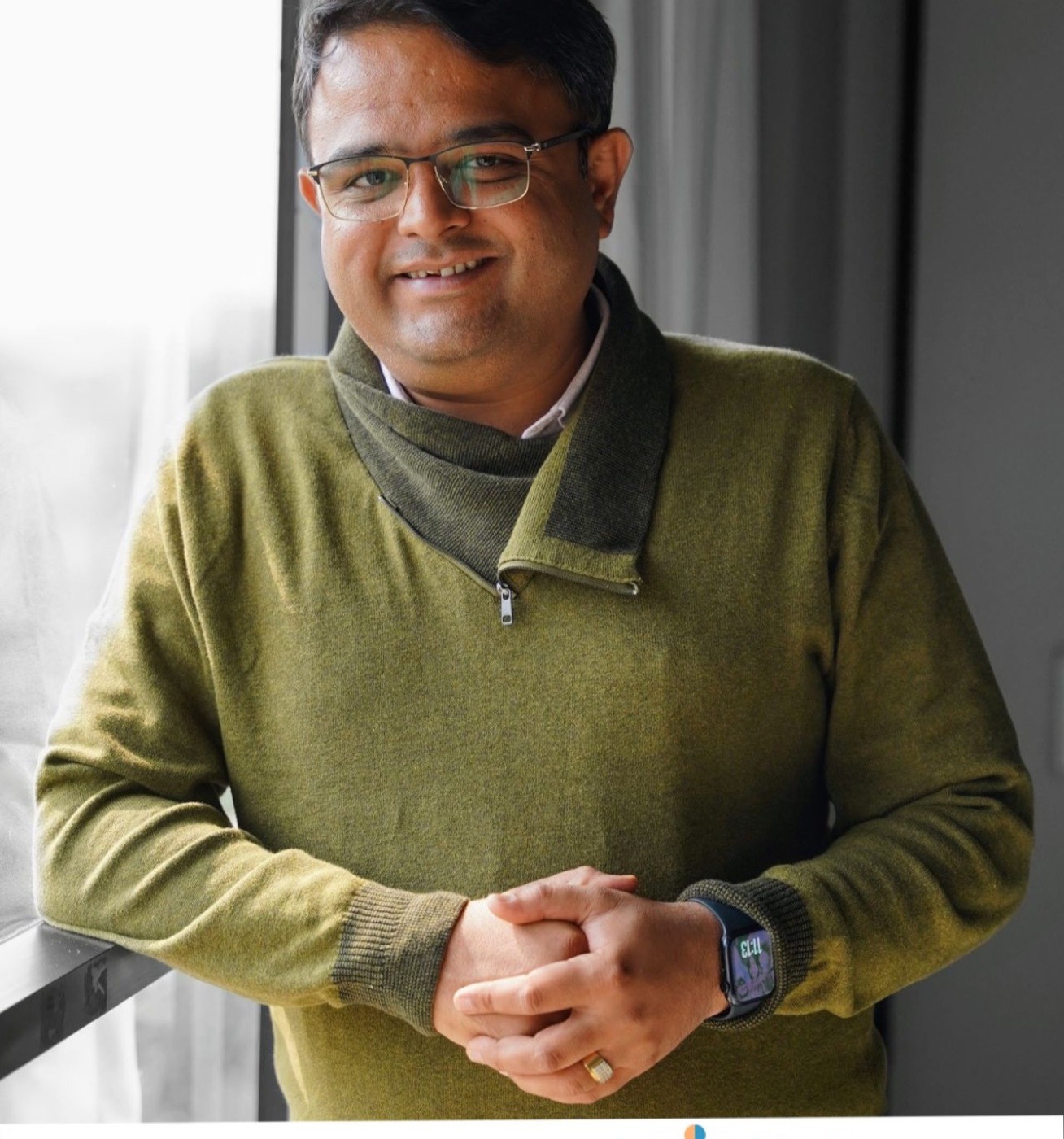 Portrait of a man in a green sweater, smiling, leaning against a window